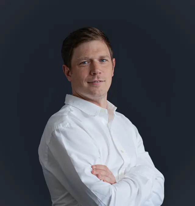 Businessporträt eines Mannes mit verschränkten Armen, leicht seitlich stehend, aufgenommen in einem modernen Innenraum beim Kunden in München.
