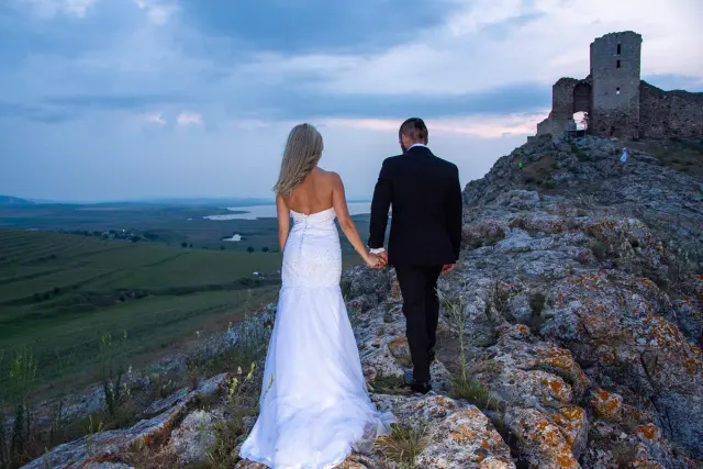 The bride and groom walk together across a scenic rocky hill during their Trash the Dress session at Enisala Ruins.
