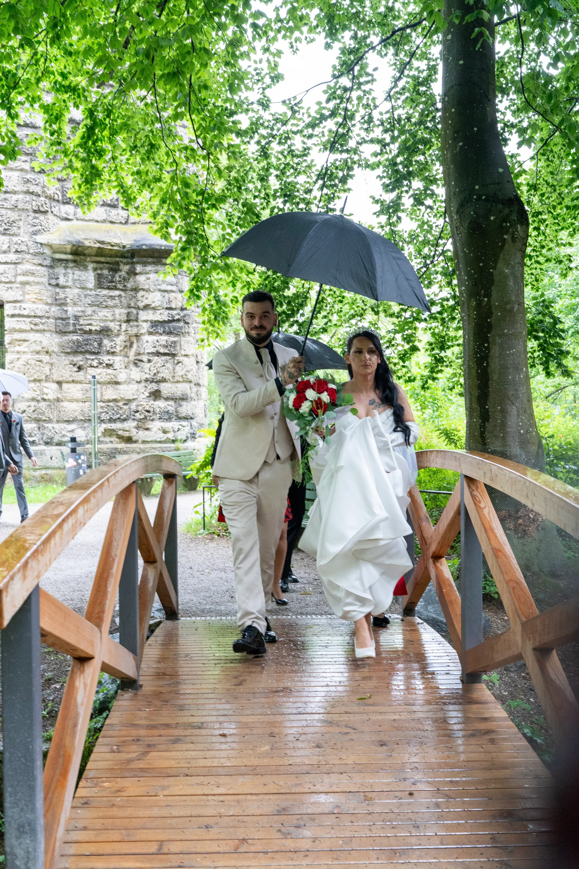 Bride and groom crossing the wooden bridge at the Mutterturm in Landsberg under an umbrella