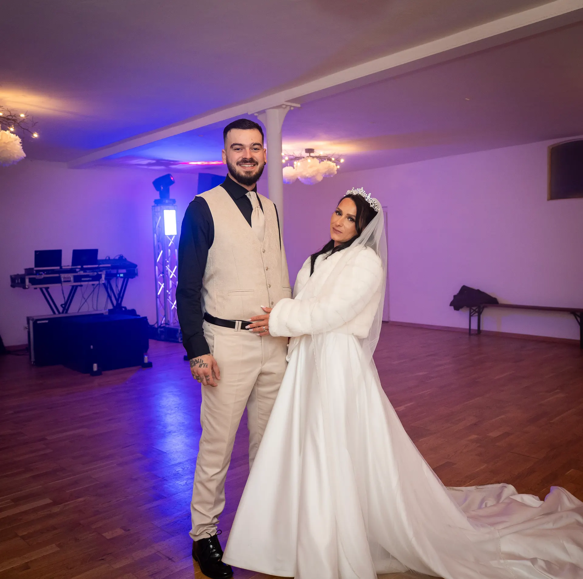 Bride and groom in the reception hall, the DJ booth in purple light behind them