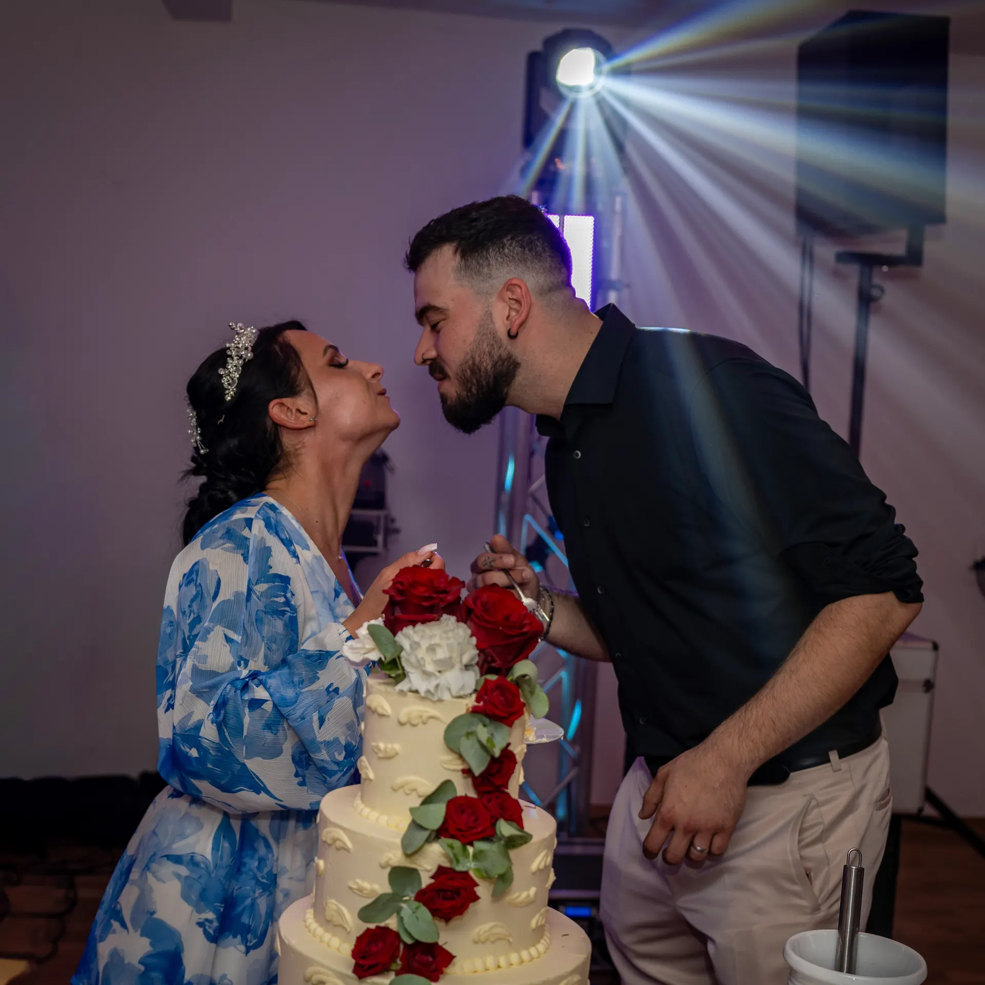 Bride in a blue floral dress and groom leaning in for a kiss at the wedding cake