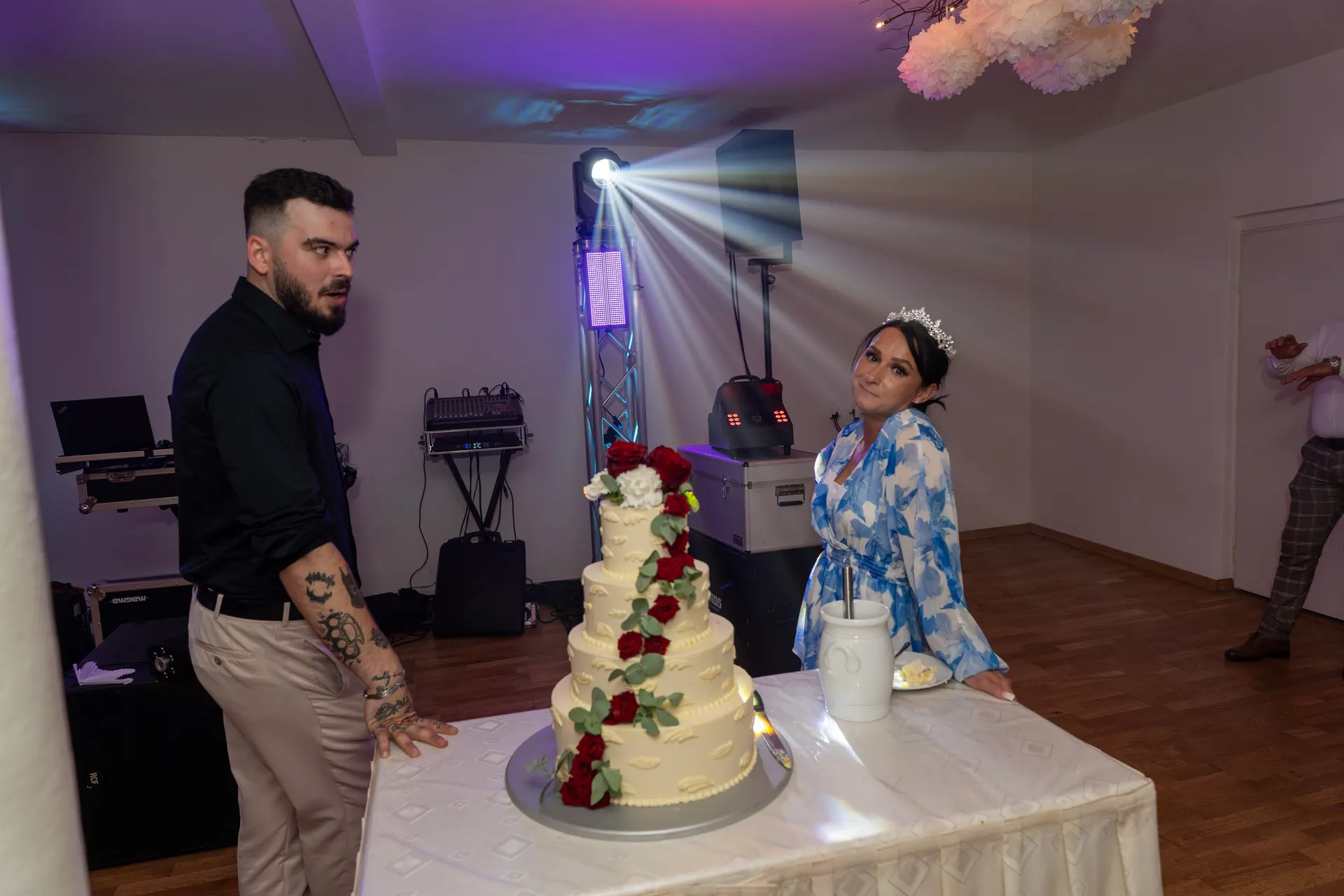 Bride and groom at the wedding cake with red roses, light beams from the DJ rig behind