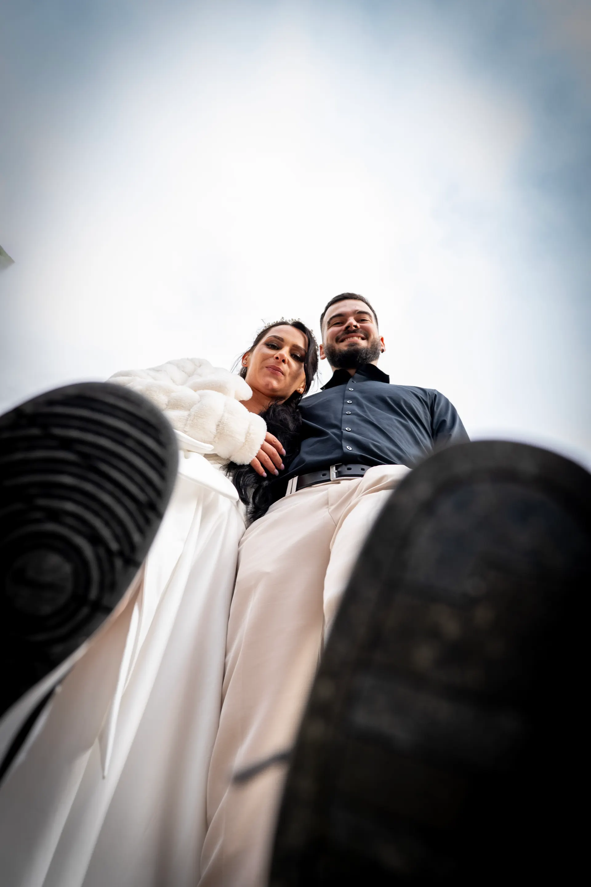 Bride and groom laughing into the camera, shot from below between their shoe soles