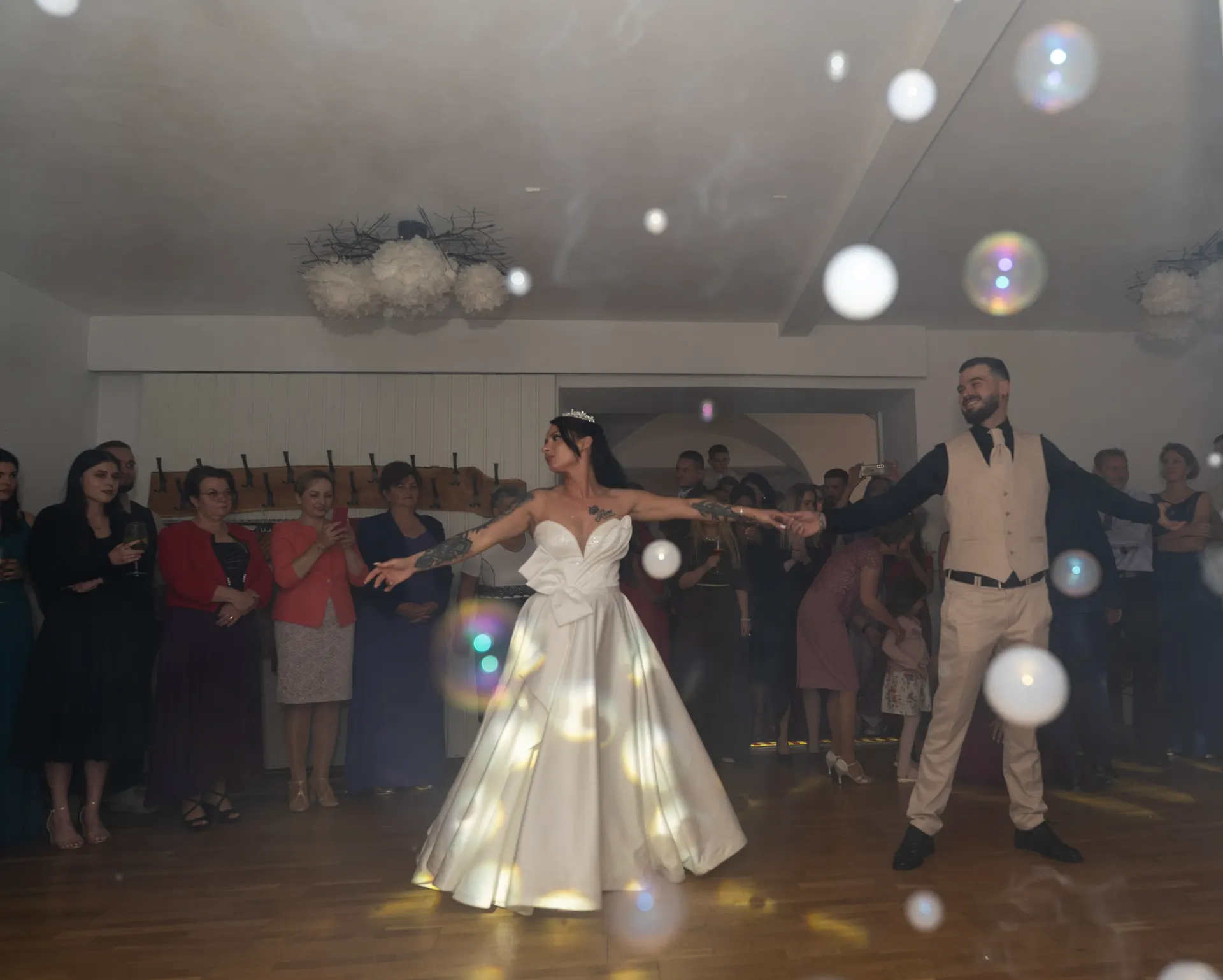 Bride and groom dancing among soap bubbles, guests watching in a circle