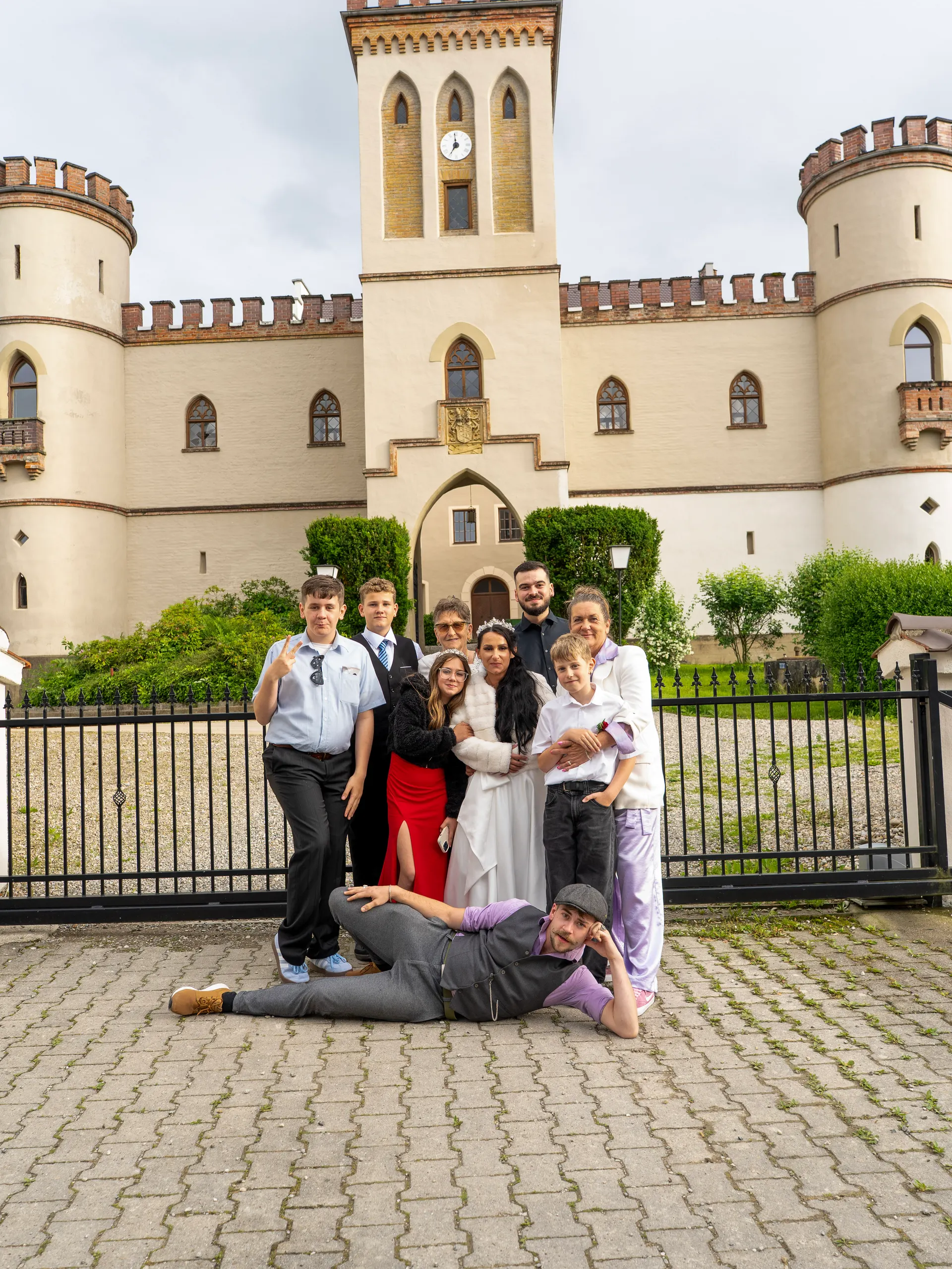 Wedding party posing playfully in front of the gate of Schloss Igling