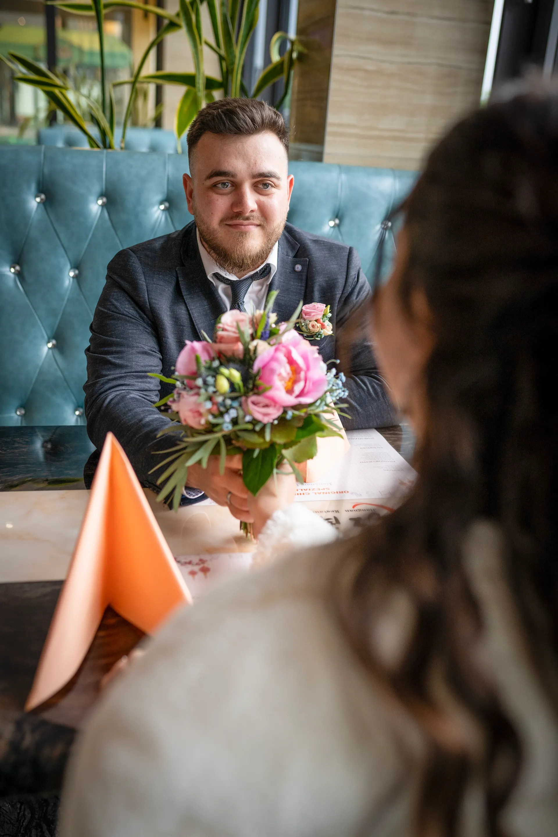 Groom holding the bouquet in the restaurant, smiling at the bride