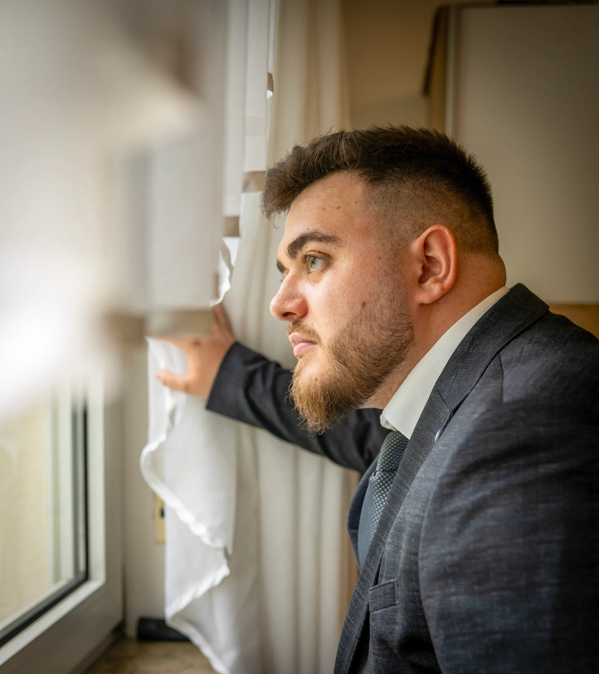 Groom in a dark suit looking out of the window before the ceremony