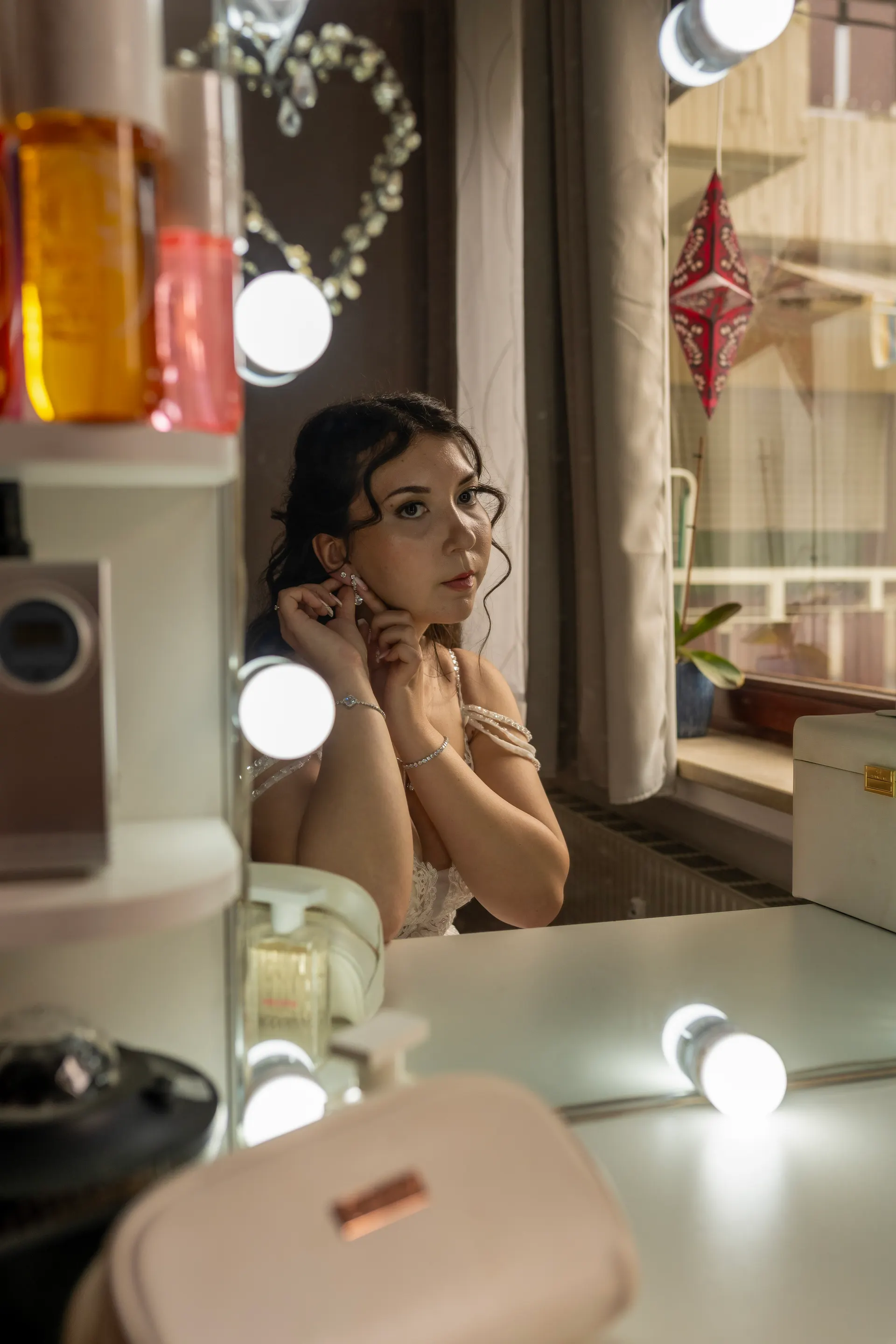 Bride putting on her earrings at a lit vanity table