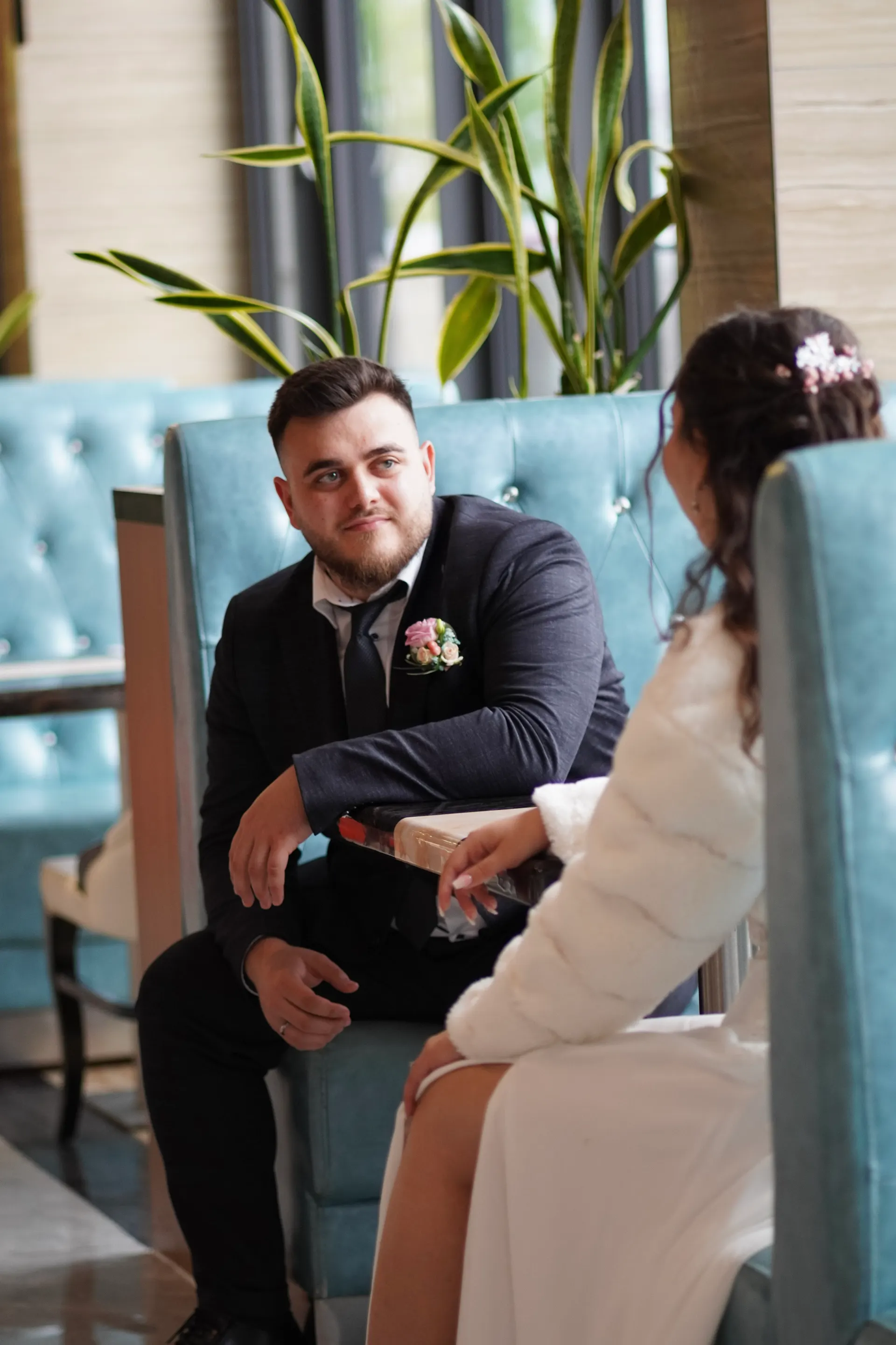 Bride and groom sitting opposite each other on turquoise velvet benches