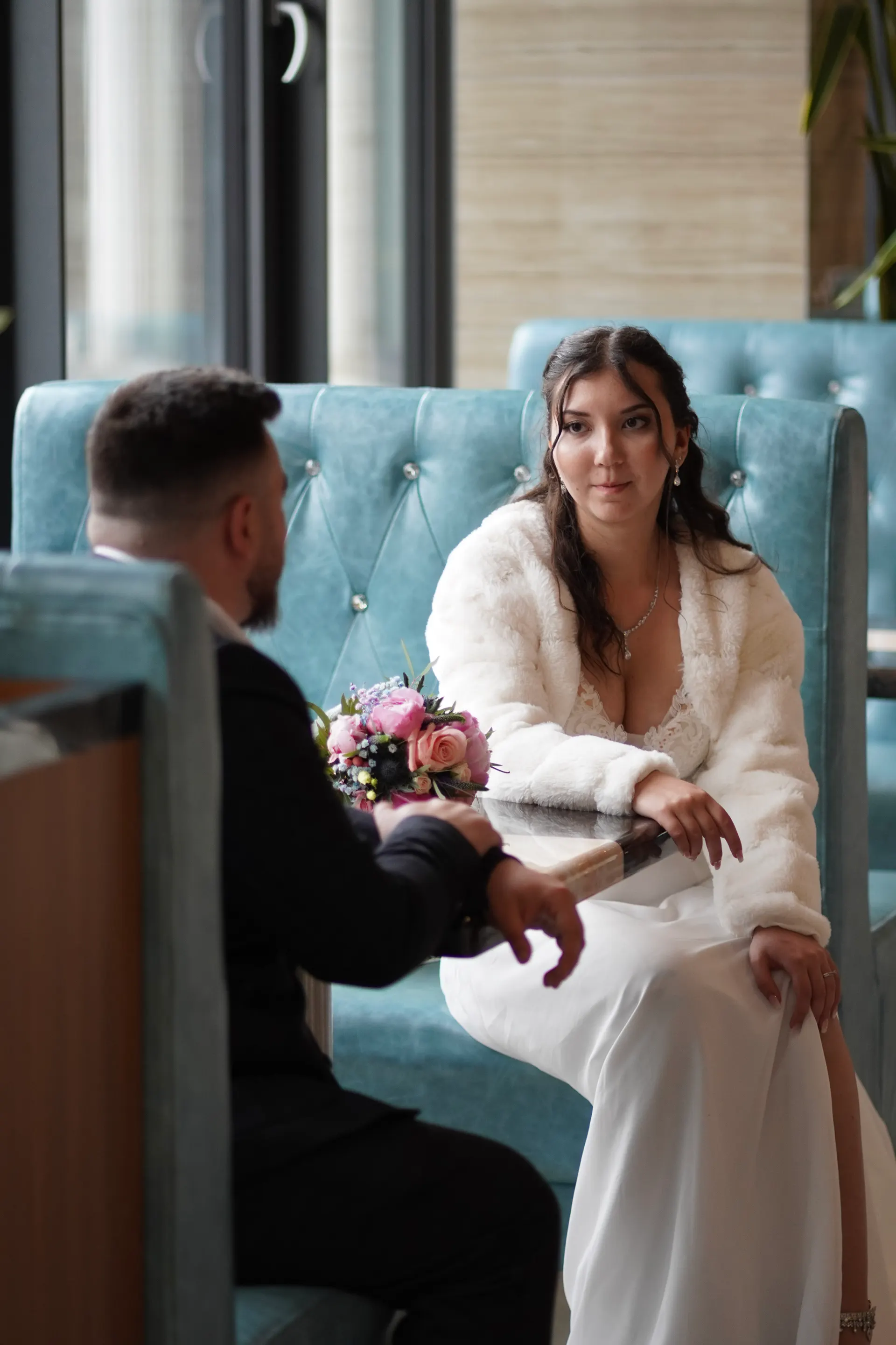 Bride in a faux-fur jacket talking to the groom in the restaurant