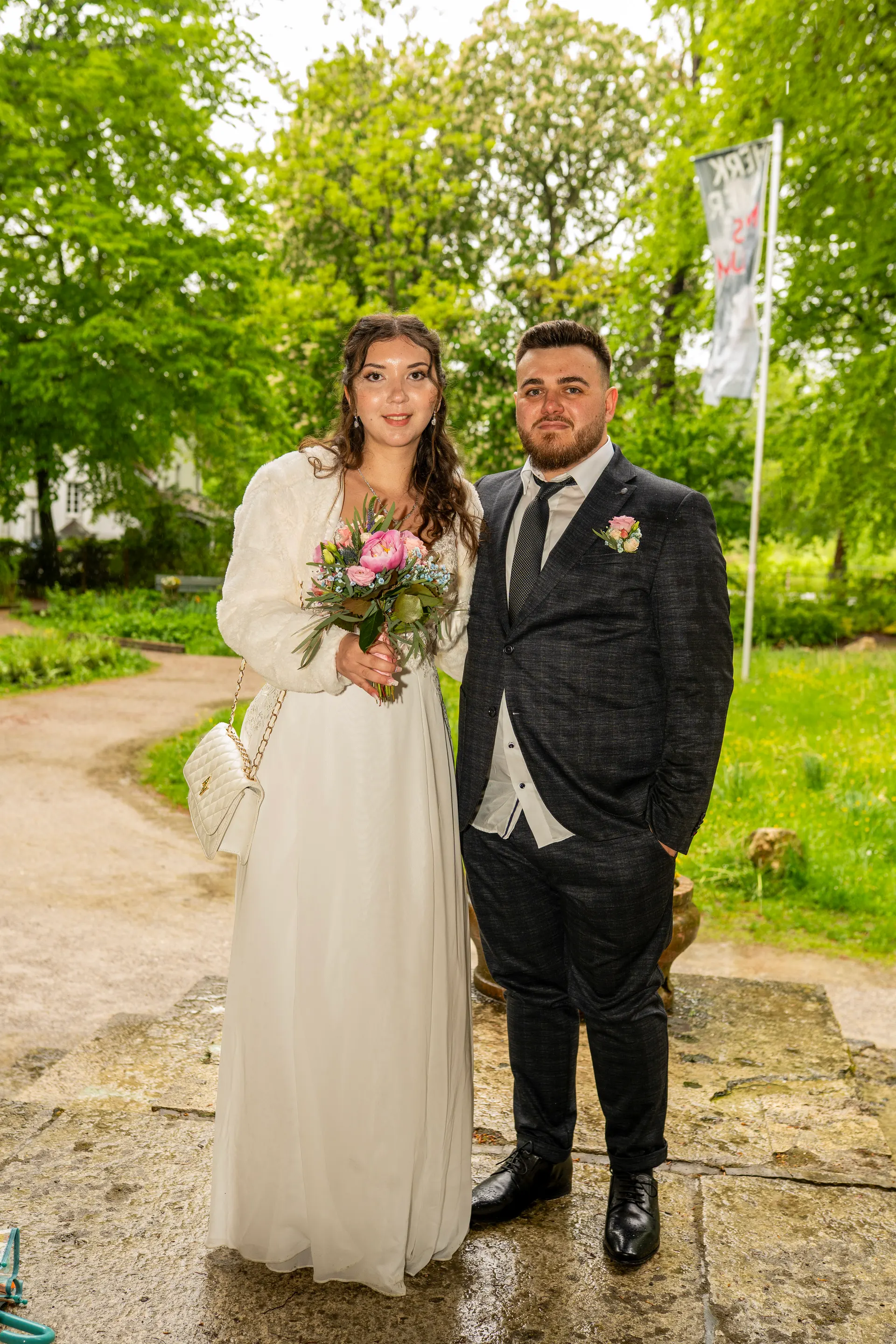 Bride and groom with a pink bouquet in a park, she in white, he in a checked suit